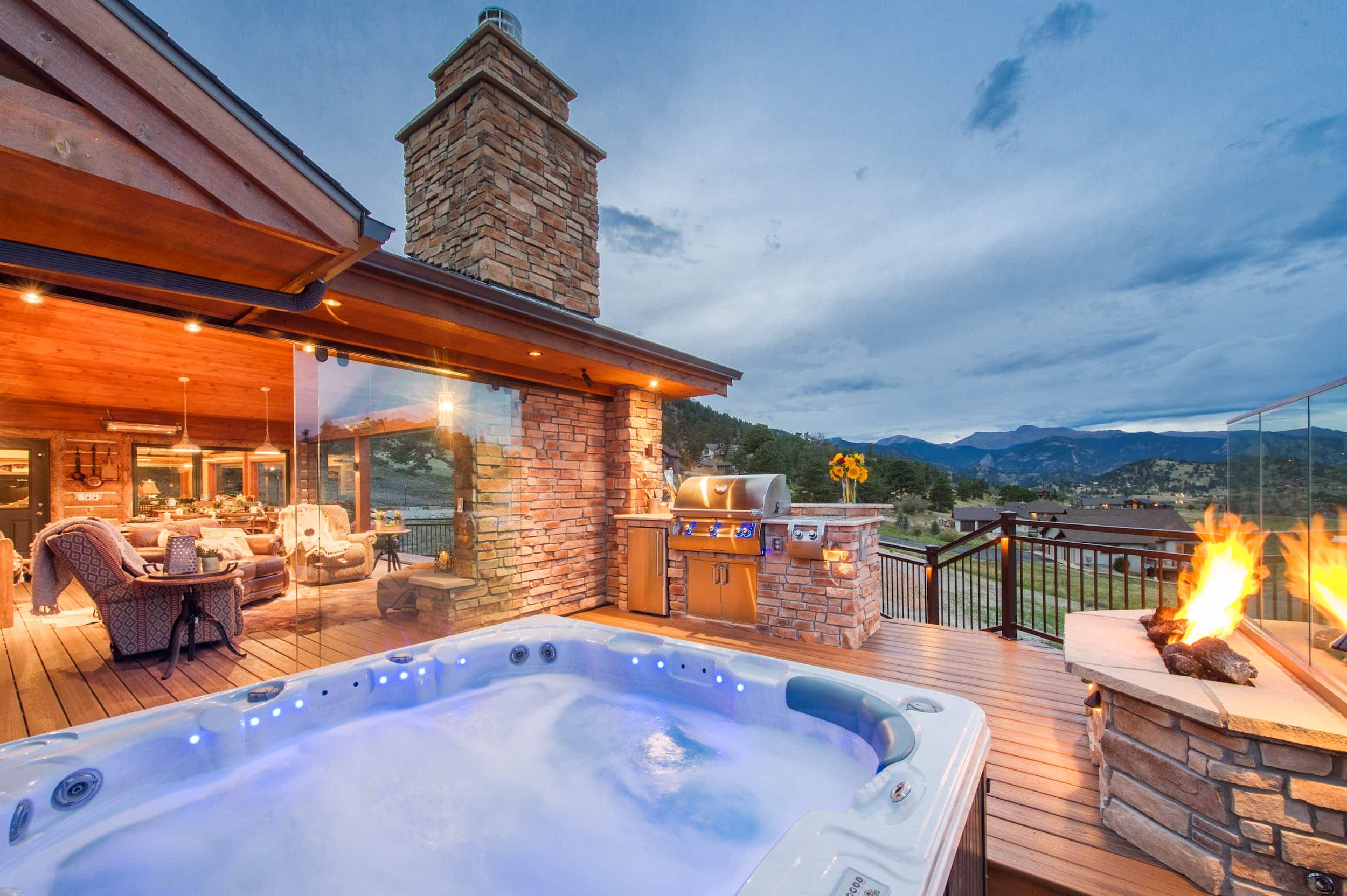 A hot tub on a deck with a grill and a fireplace.