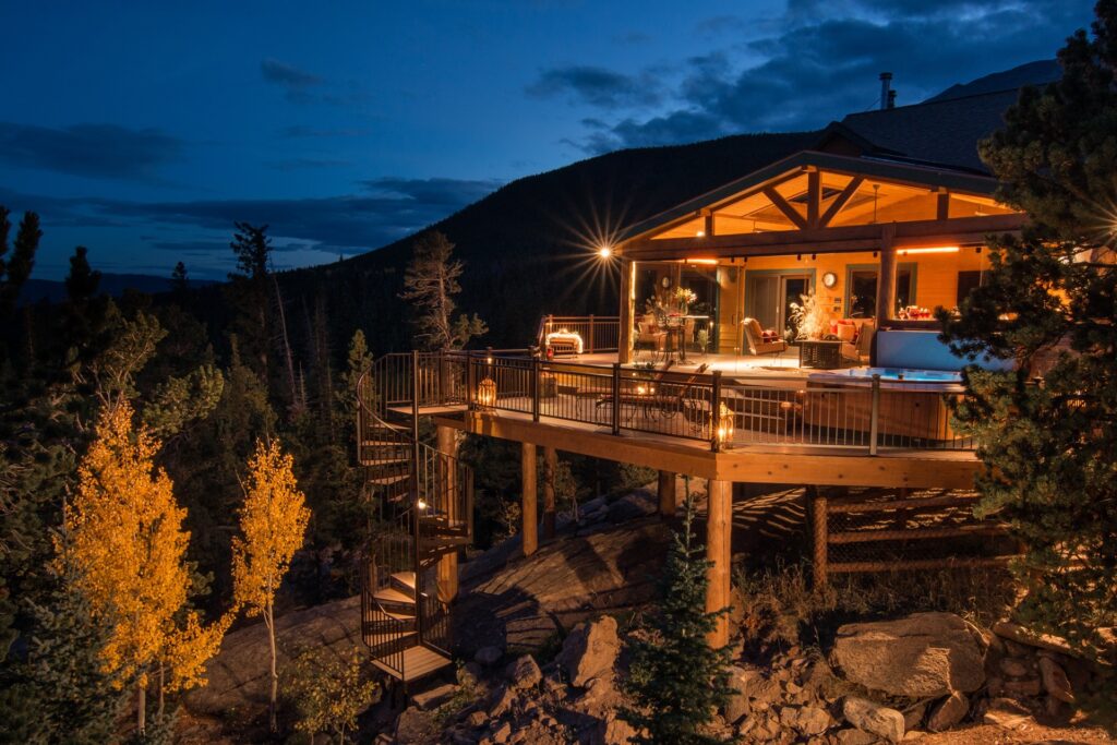 A deck with a hot tub and a spiral staircase at night. There's a mountain in the background.