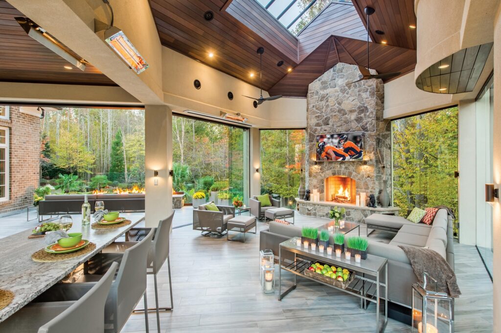 Inside a covered deck with a fireplace and glass walls. Outside is a view of trees.