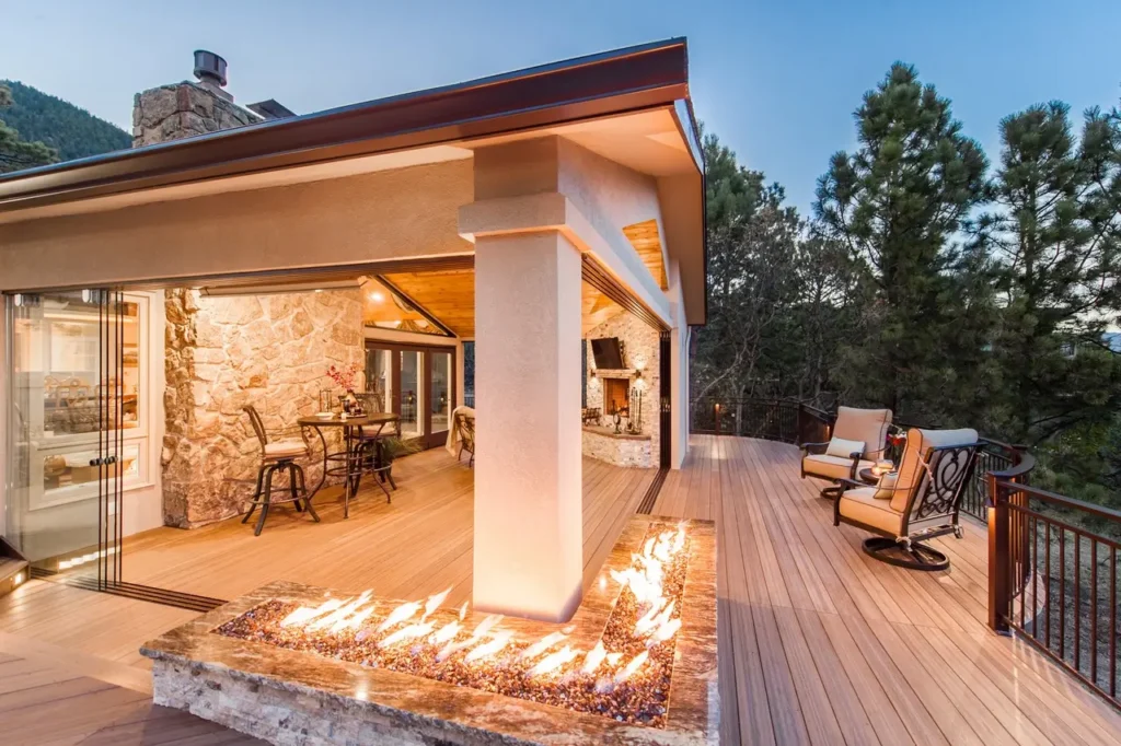 Modern deck in Colorado Springs with fire feature at dusk, adjacent to a cozy outdoor seating area and dining space. Surrounded by trees, it conveys warmth and luxury.
