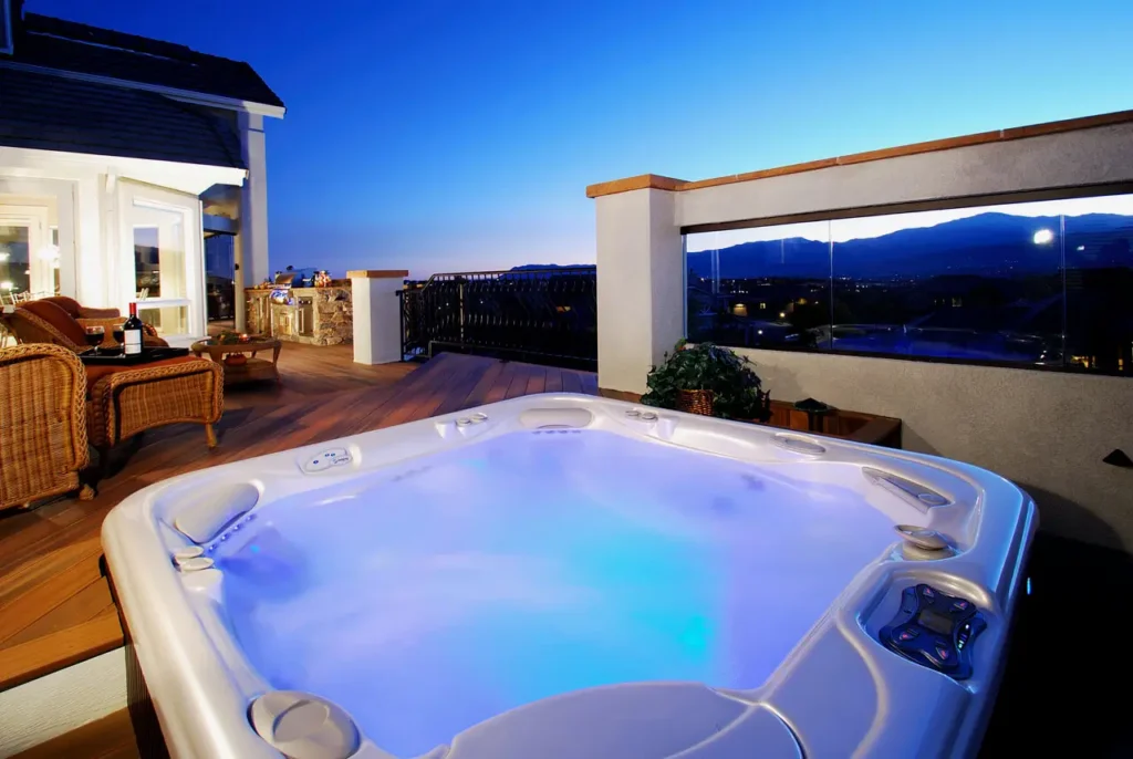 Outdoor hot tub on a wooden deck in Colorado Springs at sunset, with glowing blue water. Rattan furniture and a mountain view create a serene, luxurious ambiance.