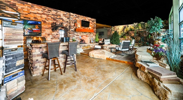 Spacious showroom in Louisville with stone walls and floor, featuring a cozy bar area with stools, a lounge with patio chairs, and lush indoor plants, evoking a rustic, inviting ambiance.